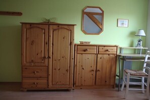 Ein Zimmer mit einem Holzschrank, einem Schreibtisch mit Stuhl, einer Lampe und einem gerahmten Spiegel an der Wand.