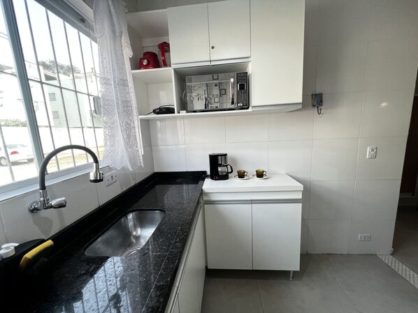 A modern kitchen with a black countertop, white cabinets, a stainless steel sink, and a window with a view of the outside.