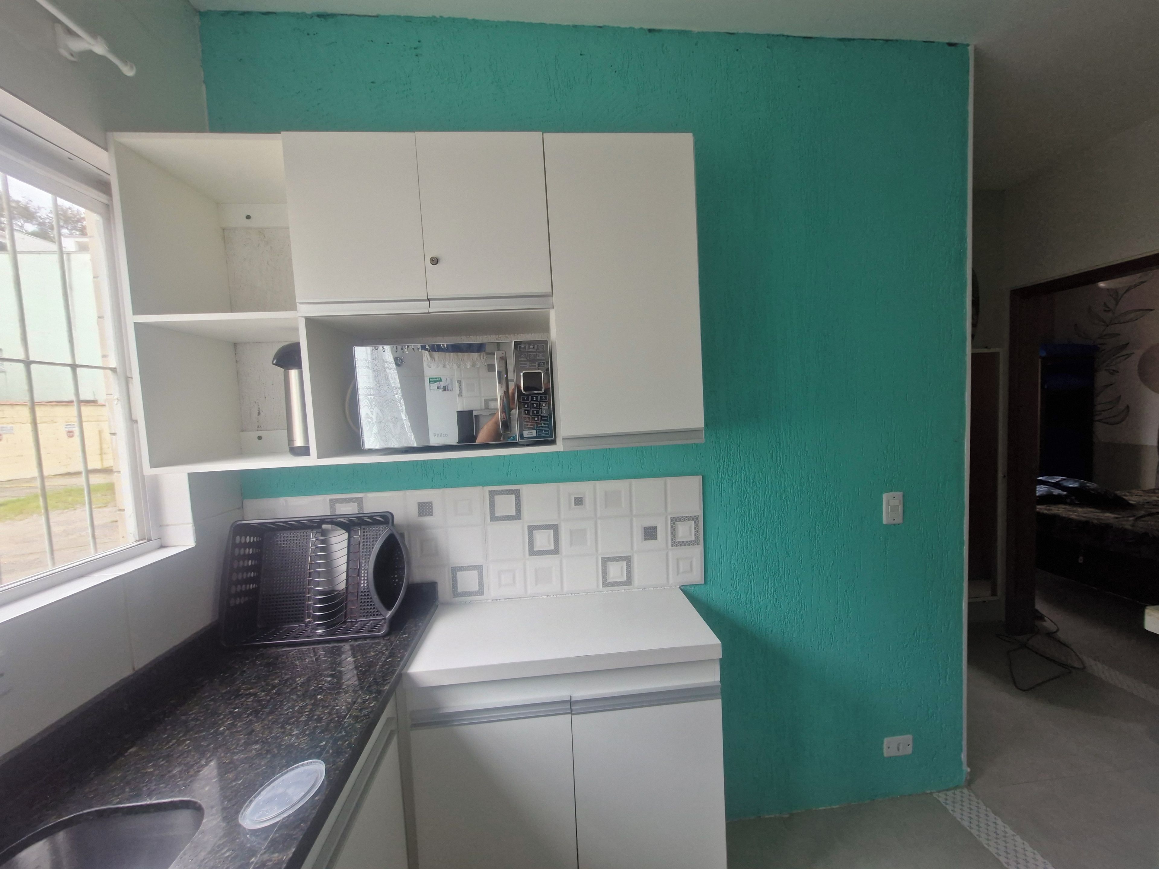 Cozinha compacta com micro-ondas, pia e pequena geladeira.