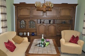 Ein Wohnzimmer mit einem Holzschrank, zwei Sesseln, einem Couchtisch und einer Kandelaber.
