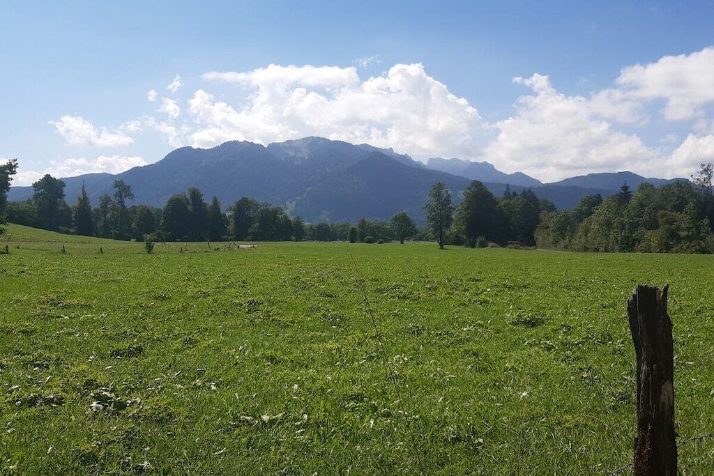 A grassy field with a wooden post in the foreground and mountains in the background.