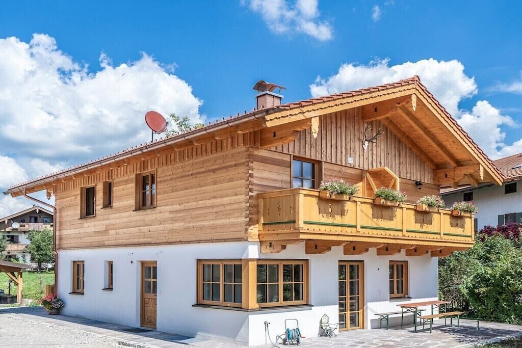 A two-story wooden chalet with a balcony, a satellite dish, and a stone patio.