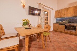 Ein Essbereich mit Holztisch und -stühlen, einer Blumenvase, einem an der Wand befestigten Fernseher und Küchenschränken.