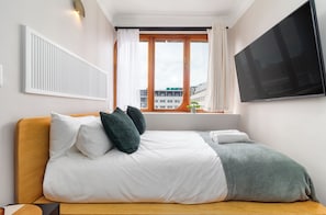 A hotel room with a bed, a TV, a window with curtains, and a view of buildings outside. - Charlie and the Chairman | Modern CBD Apartment (Cape Town)