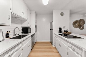 Eine moderne Küche mit weißen Schränken, einer schwarzen Induktionskochplatte, einem Edelstahlkühlschrank und einer Mikrowelle.