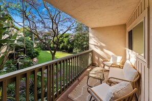 A balcony with a view of a garden, a table with chairs, and a window. - Hang Ten Hideaway by Coastline Vacation Rentals (San Diego)