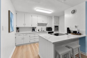 A modern kitchen with white cabinets, a central island, a microwave, an oven, and a sink. - Hang Ten Hideaway by Coastline Vacation Rentals (San Diego)