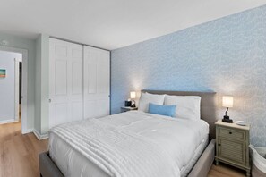 A bedroom with a bed, two bedside tables with lamps, a wardrobe, and a patterned wall. - Hang Ten Hideaway by Coastline Vacation Rentals (San Diego)