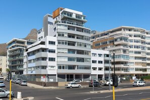 Un immeuble à plusieurs étages doté de balcons, une rue devant et des voitures garées le long de la chaussée.