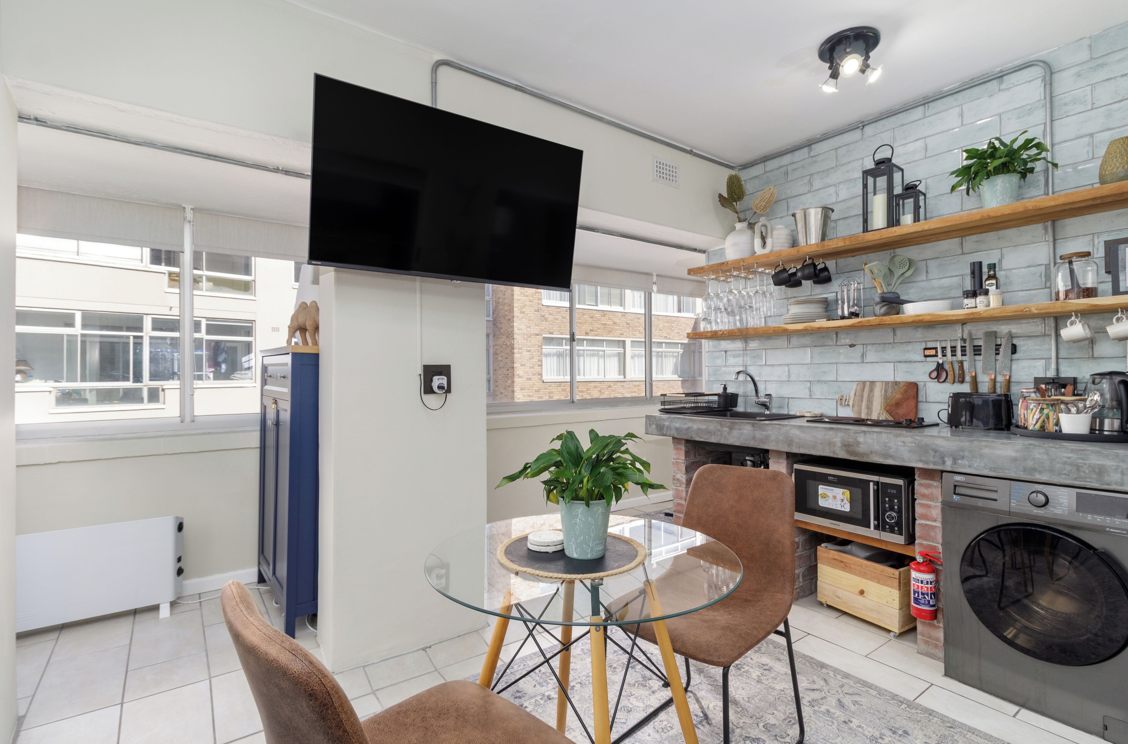 A modern kitchen with a built-in oven, a washing machine, and a dining area with a glass table and chairs.