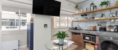 Une cuisine moderne équipée d’un four encastré, d’un lave-linge et d’un coin repas avec une table et des chaises en verre.