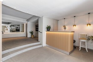 Un espace d’accueil avec un comptoir de réception en bois, une chaise blanche et une plante en pot.