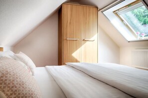 A bedroom with a sloped ceiling, a wooden wardrobe, a bed with white bedding, and a skylight. - Holiday apartment with 1 bedroom (Ostseebad Prerow)