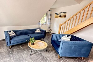 Ein Wohnzimmer mit zwei blauen Sofas, einem Holztisch und einer Treppe.