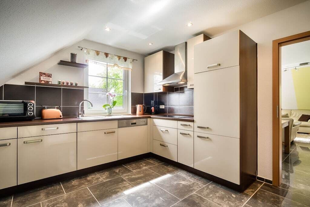 A modern kitchen with a built-in oven, a sink, and a window with a view of greenery.