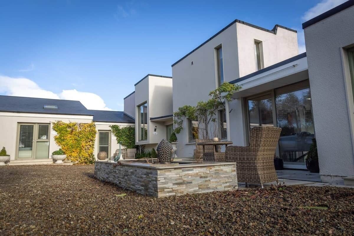 Un moderno edificio residencial con un patio de piedra, mobiliario exterior y cielo despejado.