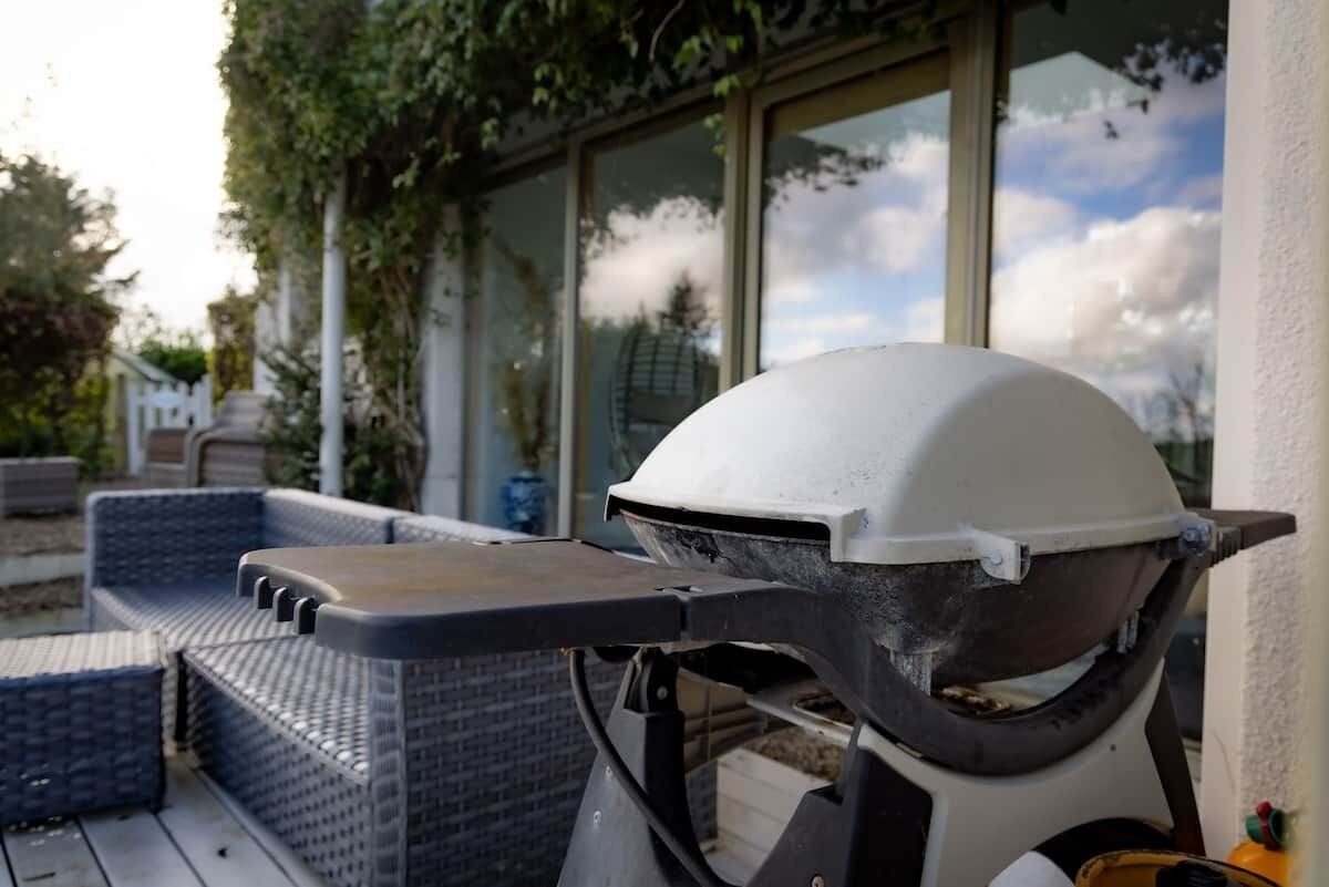 Een barbecue op een terras buiten, met wicker meubels en een glazen deur op de achtergrond.