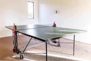 A ping pong table with wheels in a room with a concrete floor and a window.