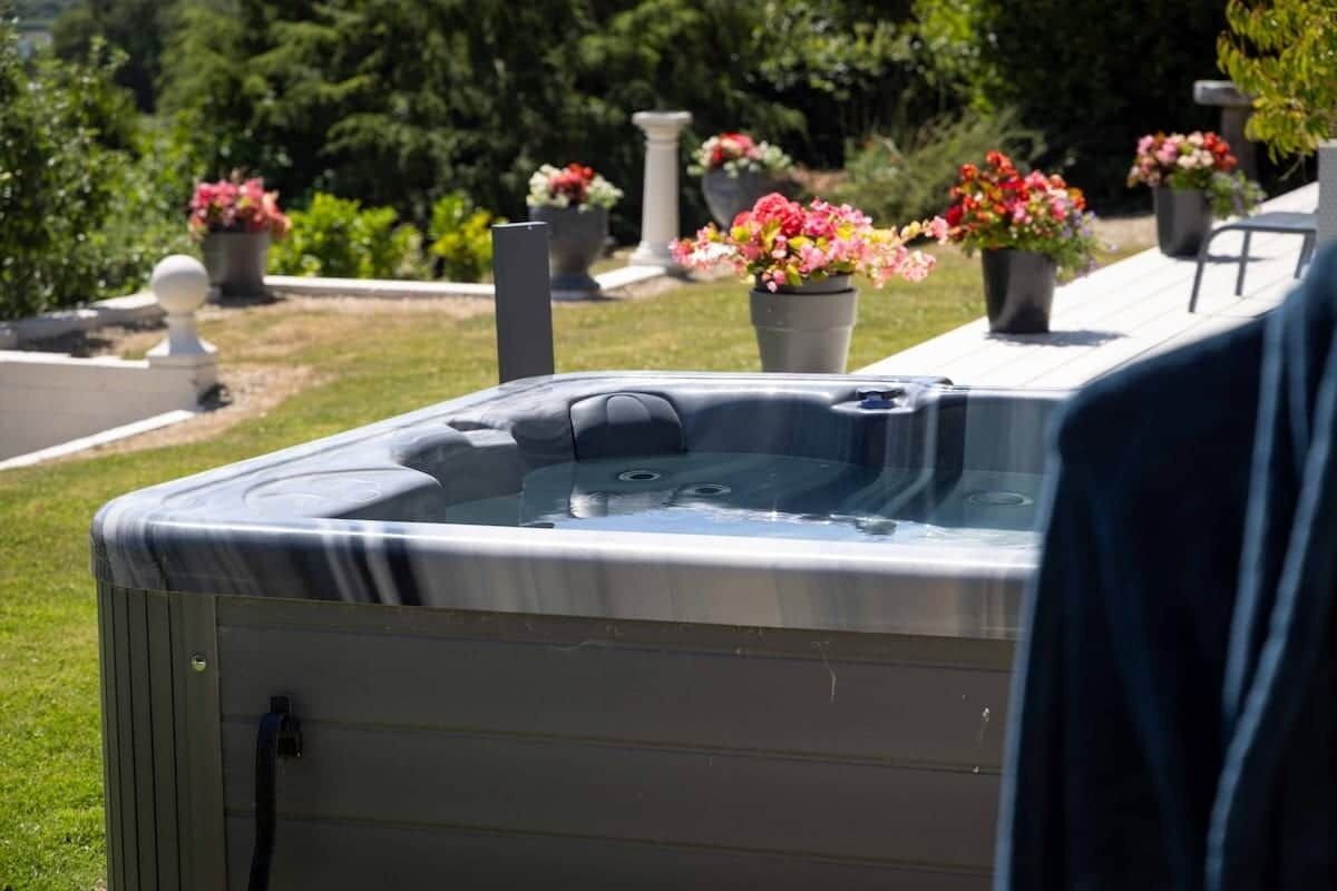 A hot tub in an outdoor setting with a garden and potted plants in the background.