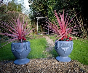Two large decorative planters with a geometric design, placed on a gravel path in a garden setting.