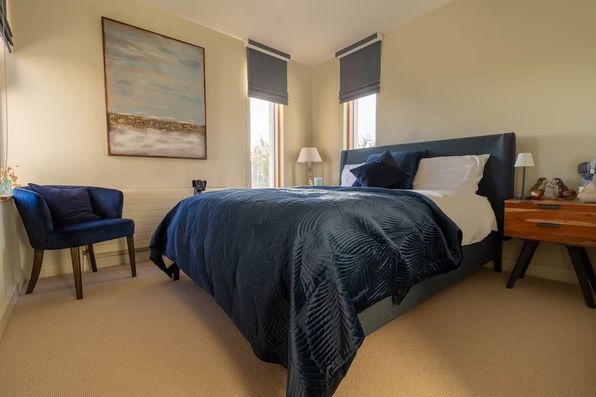 A bedroom with a bed, a chair, a nightstand, and a painting on the wall.