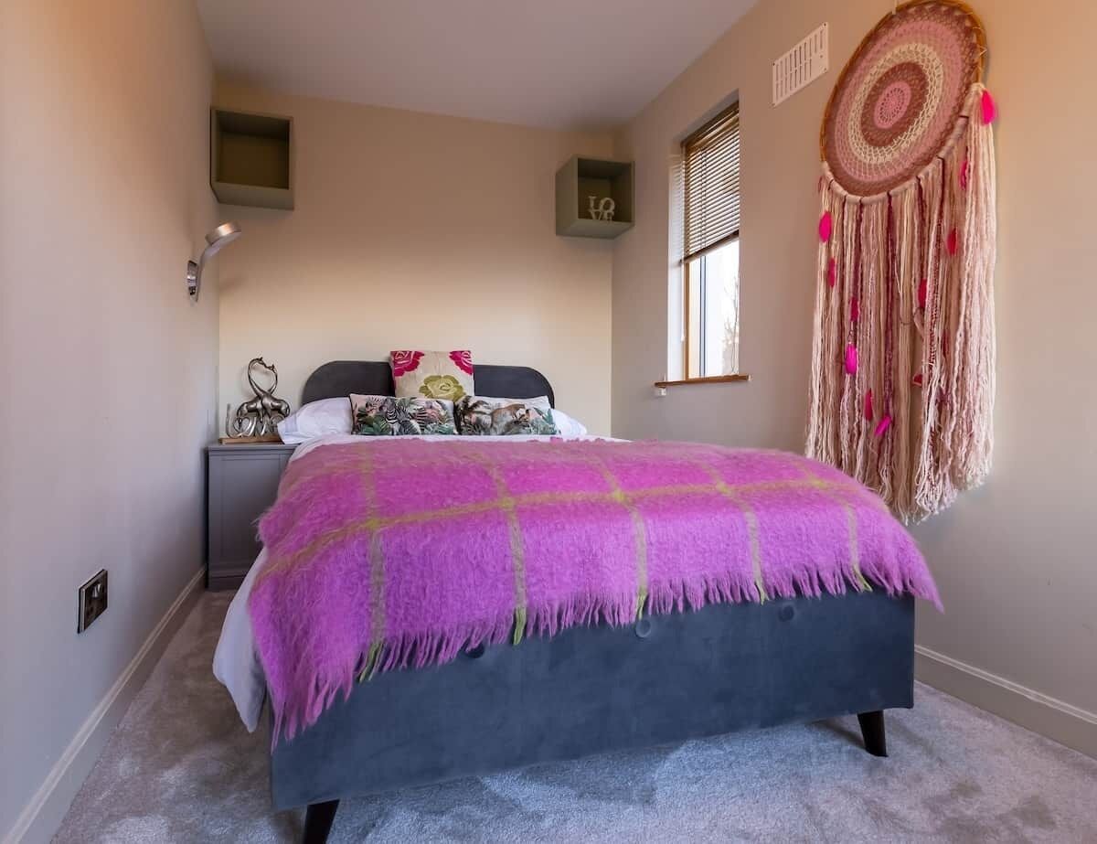 Un dormitorio con cama, mesita de noche, decoración en la pared y una ventana.
