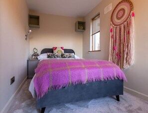 A bedroom with a bed, bedside table, wall decor, and a window.