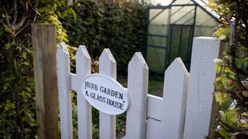 A white picket fence with a sign that reads 'Herb Garden & Glass House.'