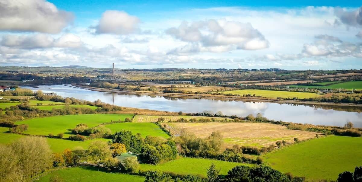 Een rivier met een brug, groene velden en een verre toren.