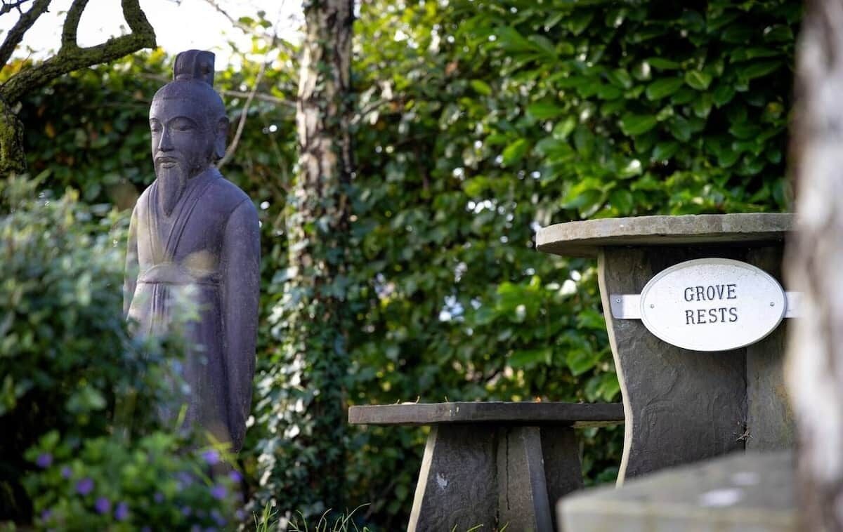 Una statua in un giardino con un cartello che riporta la scritta 'Grove RESTS'.