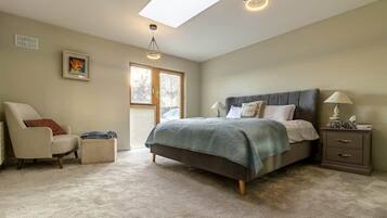 Une chambre à coucher comprenant un lit, une chaise, une table de chevet, une lampe, un tableau au mur et un puits de lumière.