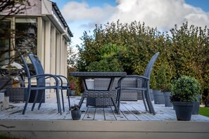 An outdoor patio with a table and chairs, surrounded by potted plants and a hedge.