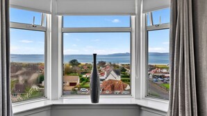 A bay window with a clear view of a coastal landscape, including houses and a body of water. - Stunning  villa for 8 people with WIFI and terrace (Ardrossan)