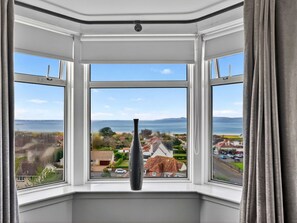 A bay window with a clear view of a coastal landscape, including houses and a body of water. - Stunning  villa for 8 people with WIFI and terrace (Ardrossan)