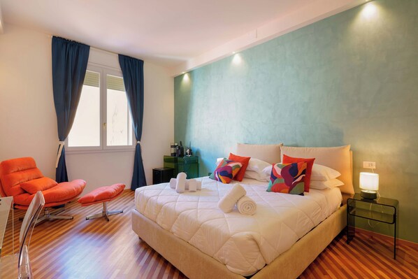 Habitación de hotel con una cama grande, una silla, un escritorio y un ventanal con cortinas.