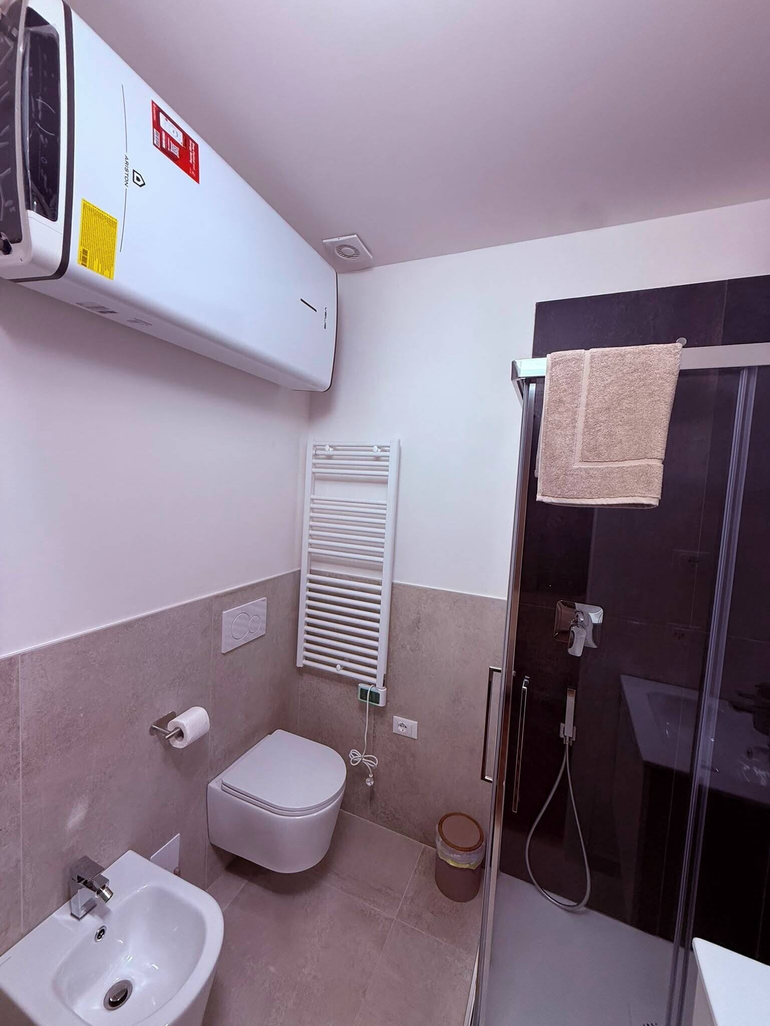 Un baño con inodoro, bidé, lavamanos, toallero y cabina de ducha.