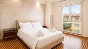 Un dormitorio con cama, piso de madera, una mesita de noche, ventana con vistas y una lámpara de pared.