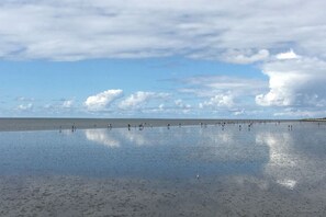 Ein Strand mit weitem Sandbereich und einem klaren Himmel mit vereinzelten Wolken.