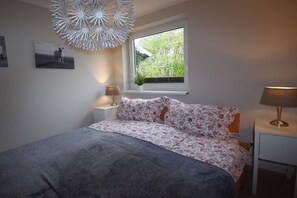 Ein Schlafzimmer mit Bett, Fenster mit Aussicht, Nachttisch mit Lampe und Wandbild.
