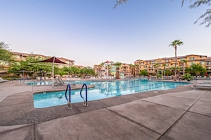 A swimming pool with lounge chairs and umbrellas, surrounded by multi-story buildings with balconies.