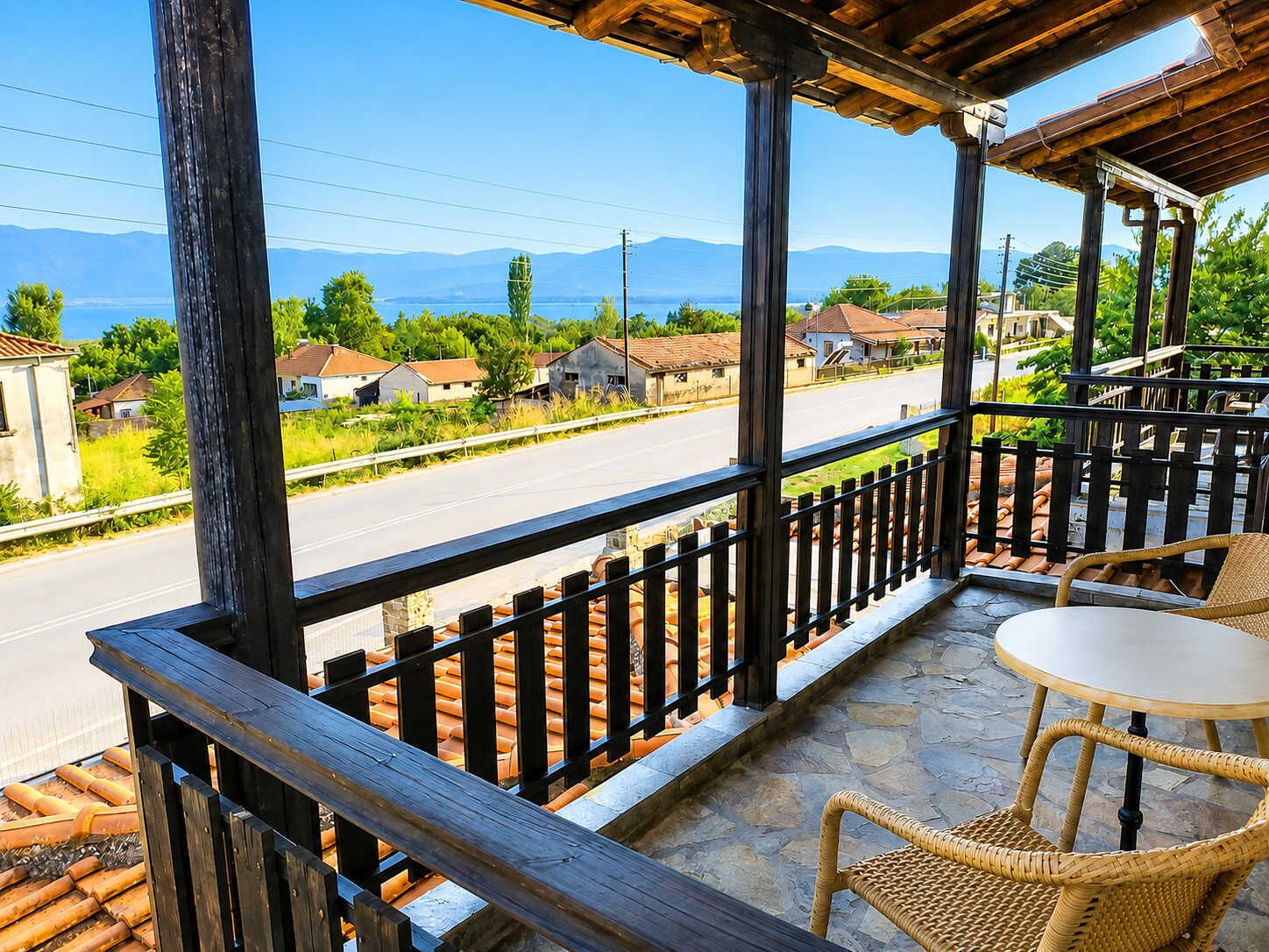 A balcony with a view of a road and houses, a table, and wicker chairs.