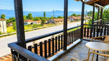 A balcony with a view of a road and houses, a table, and wicker chairs.