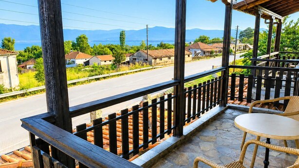A balcony with a view of a road and houses, a table, and wicker chairs. - Zidoron House - Peaceful Retreat at Lake Kerkini (Mandraki)