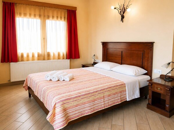 A hotel room with a wooden bed, a bedside table, a lamp, and a window with curtains.
