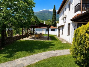 Un patio con pérgola, mobiliario exterior, un sendero de piedra y montañas al fondo.