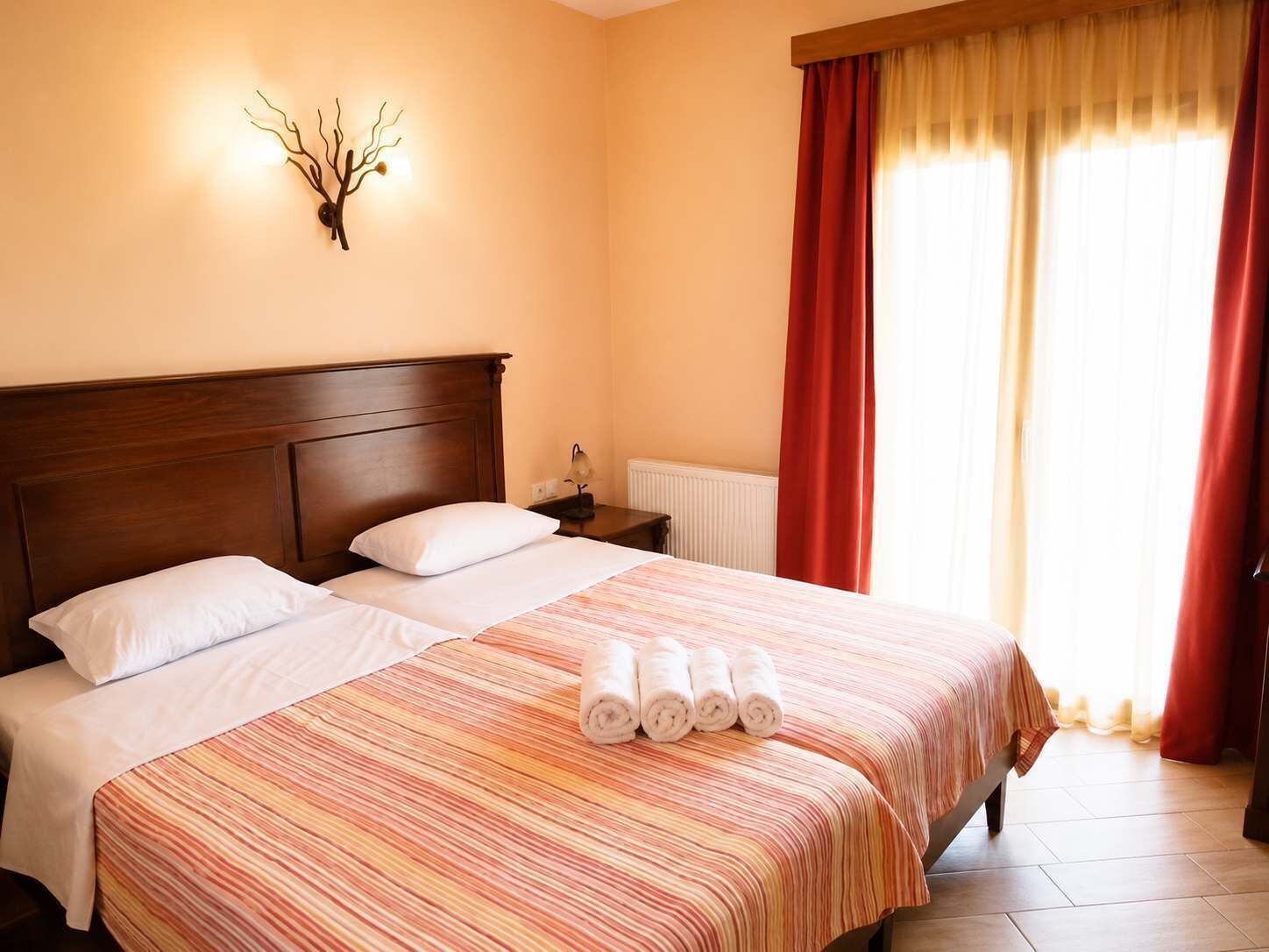 A hotel room with a large bed, two pillows, a nightstand with a lamp, and a wall-mounted light fixture.