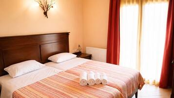 A hotel room with a large bed, two pillows, a nightstand with a lamp, and a wall-mounted light fixture.