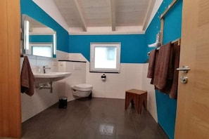 Un baño con lavamanos blanco, inodoro y un taburete de madera.