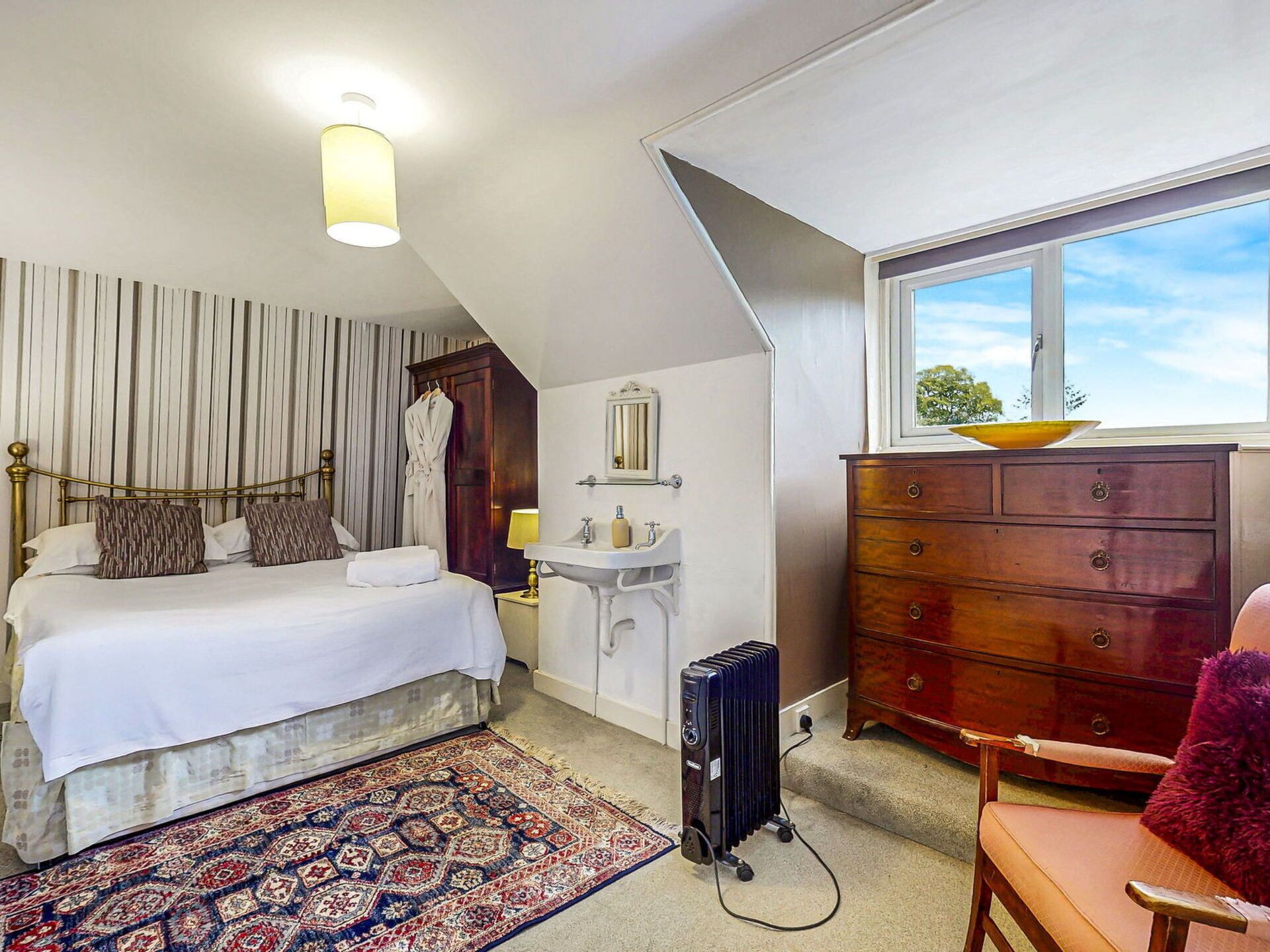 A bedroom with a bed, a dresser, a radiator, a window, and a small bathroom.