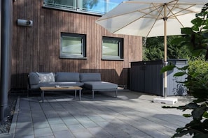 An outdoor seating area with a sofa and table, a wooden wall, and a large umbrella. - Holiday apartment in Wildeshausen with Wi-Fi (Wildeshausen)